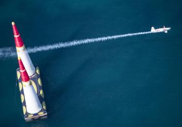 Ein Sportflugzeug fliegt zwischen zwei Pylonen und hinterlässt lange Rauchspur
