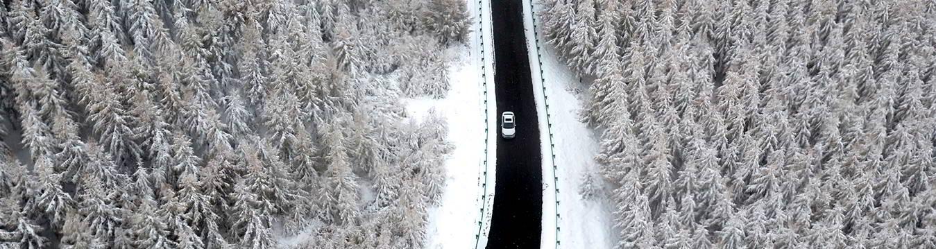 Schneelandschaft von oben mit einer Straße und einem Auto
