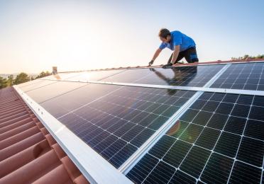 Person auf Dach mit Solarpanel und Sonne