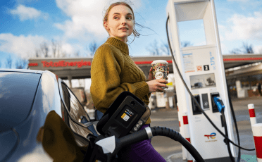 Fahrerin lädt ihr Auto und trinkt Kaffee an TotalEnergies Tankstelle